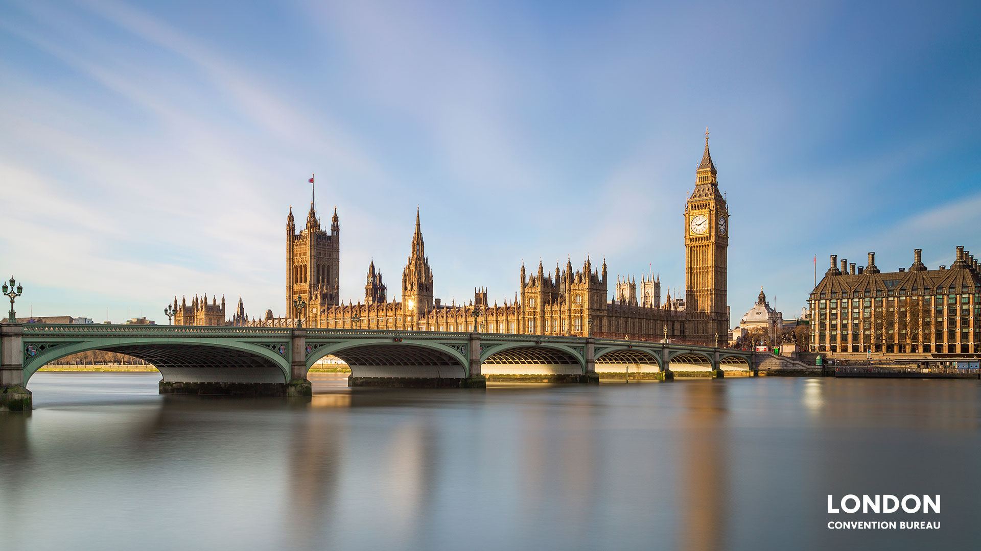 Big Ben shimmering golden at the riverfront with a big blue sky.