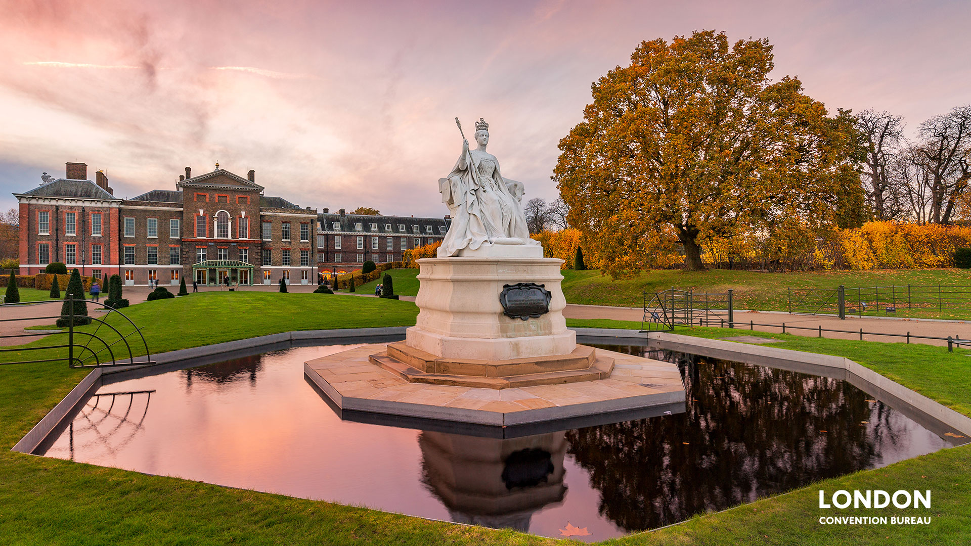 Kensington Palace at sunset, the pink clouds are reflecting in the water of a big fountain.