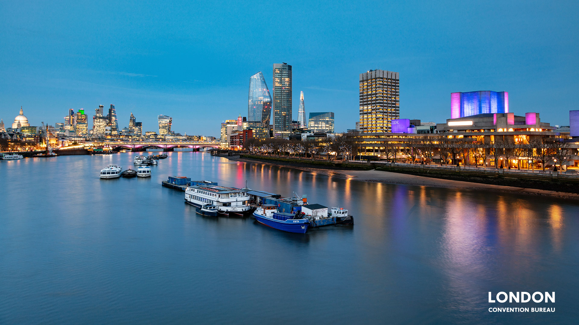 Purple and yellow lights of the buildings reflect in the river Thames in London at dusk.