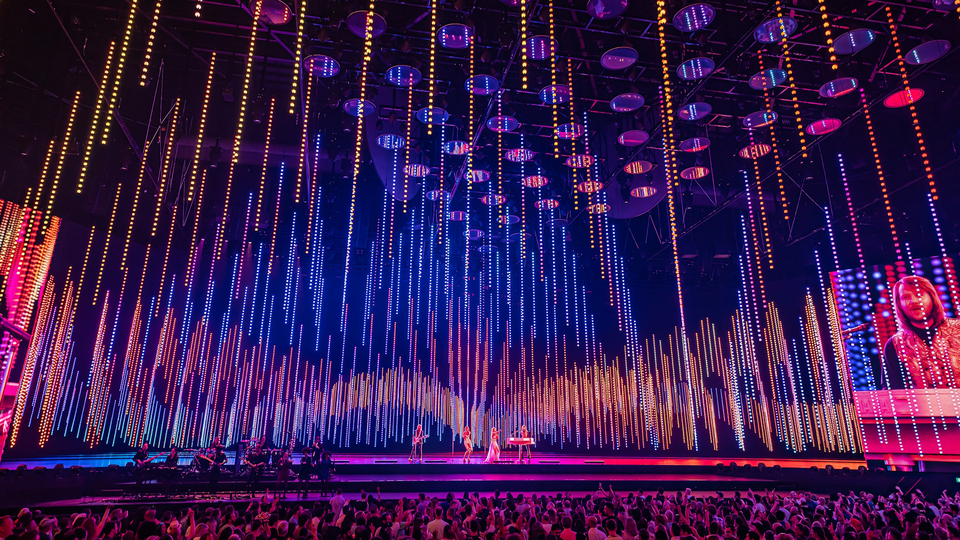ABBA Arena stage lit up in pink, orange and purple lights during a live performance of ABBA Voyage in London.
