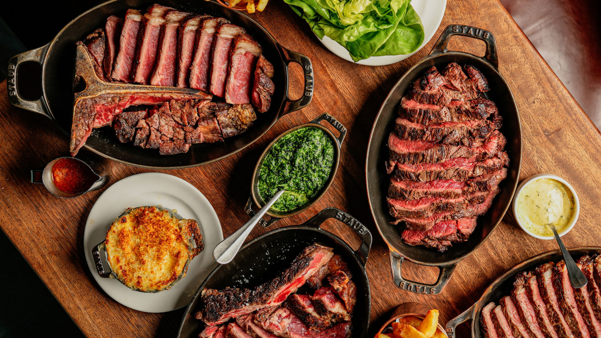 A bird's-eye photo of dishes of food at Hawksmoor with some sharing steaks and sides including macaroni cheese, salad and creamed spinach