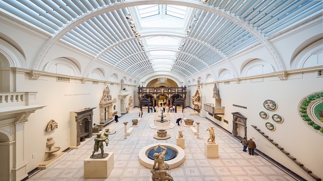 Landscape shot of the interior of the V&A Museum, with a large curved glass ceiling and various art exhibitions to look at