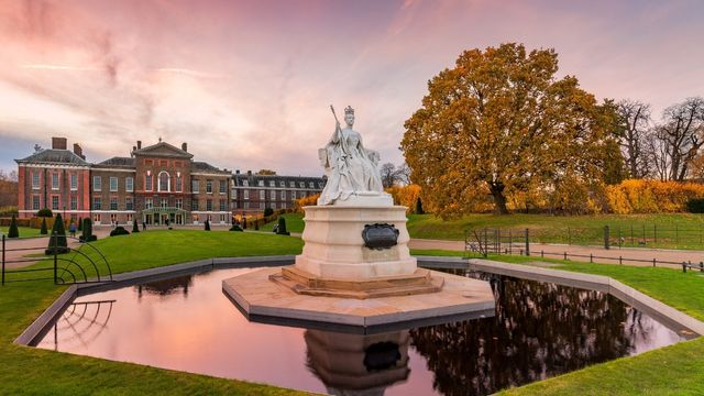 Kensington Palace and the statue of Queen Victoria. Credit: Jon Reid. Image courtesy of visitlondon.com. Queen Victoria statue in Kensington Gardens, with tree with autumn leaves, and Kensington Palace in the background