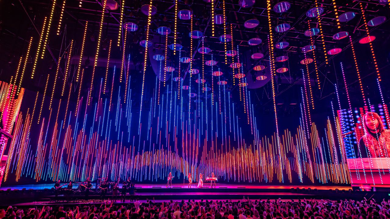 ABBA Arena stage lit up in pink, orange and purple lights during a live performance of ABBA Voyage in London.